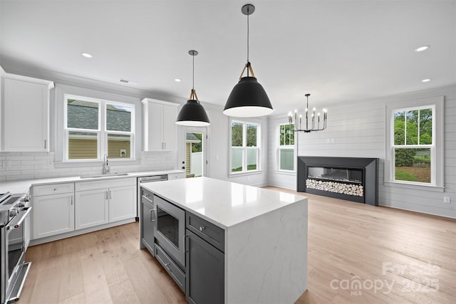 kitchen featuring a center island, decorative light fixtures, appliances with stainless steel finishes, white cabinets, and a sink