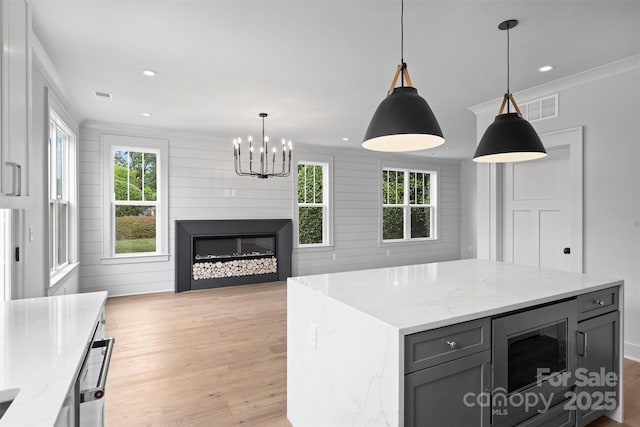 kitchen featuring light stone counters, built in microwave, light wood-style floors, a center island, and decorative light fixtures