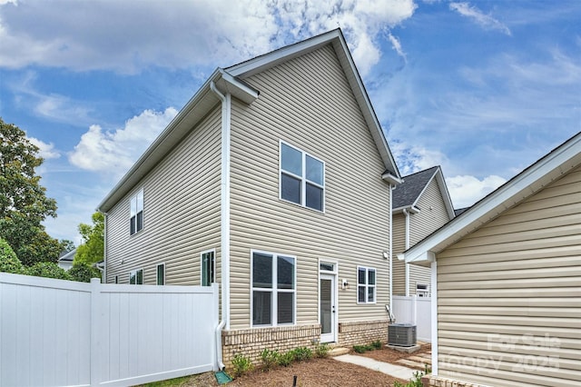 rear view of house featuring brick siding, fence, and central air condition unit