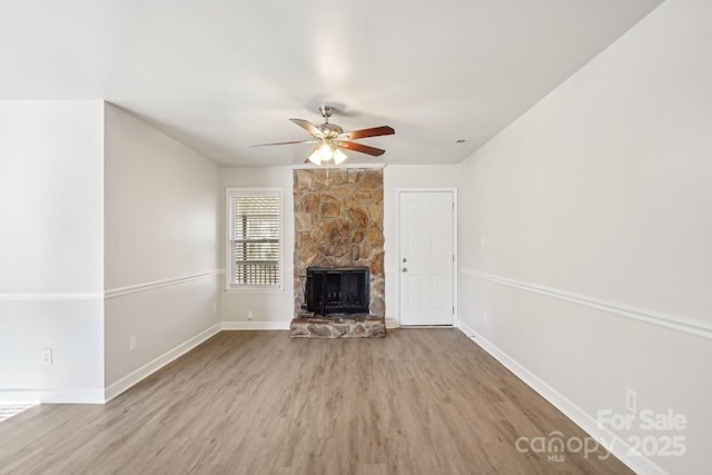 unfurnished living room with ceiling fan, a stone fireplace, wood finished floors, and baseboards