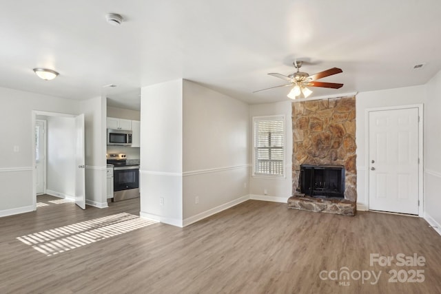 unfurnished living room with ceiling fan, a stone fireplace, wood finished floors, and baseboards