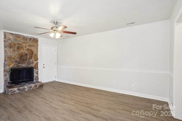 unfurnished living room with baseboards, visible vents, a ceiling fan, wood finished floors, and a stone fireplace