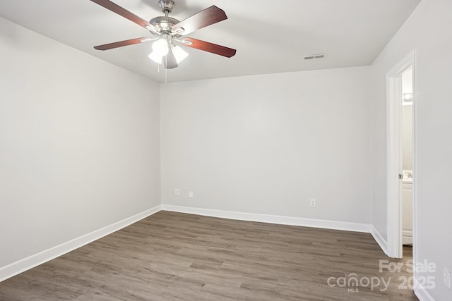 empty room with a ceiling fan, wood finished floors, visible vents, and baseboards