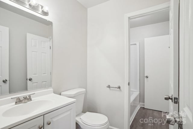 bathroom featuring toilet, baseboards, wood finished floors, and vanity