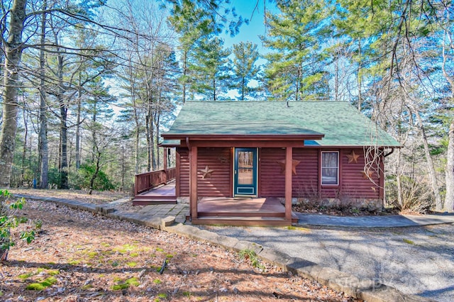 chalet / cabin with a porch, roof with shingles, and faux log siding