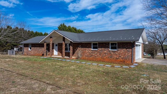 view of front facade featuring a garage, driveway, brick siding, metal roof, and a front yard