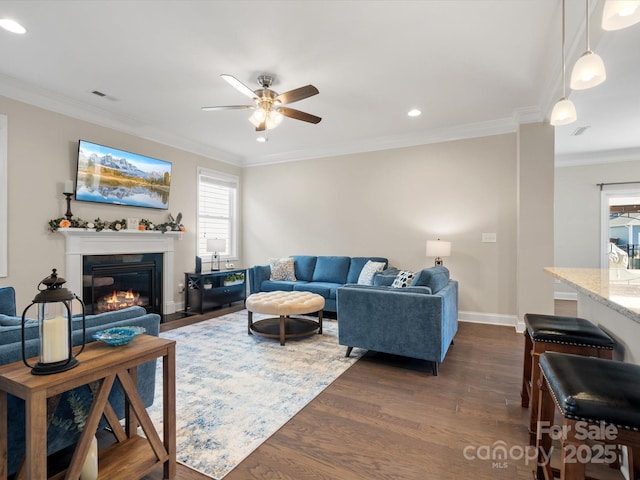 living area with crown molding, dark wood-type flooring, and a glass covered fireplace