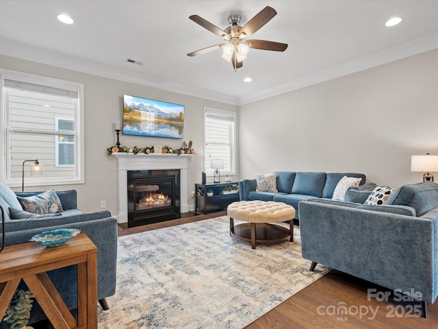 living area with a fireplace with flush hearth, visible vents, crown molding, and wood finished floors