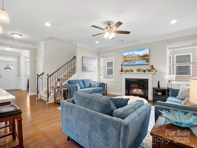 living room with a glass covered fireplace, stairway, ornamental molding, wood finished floors, and recessed lighting