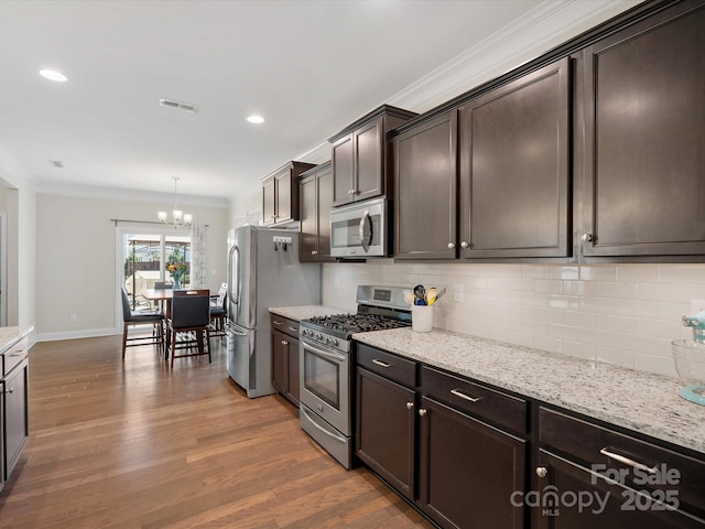 kitchen with stainless steel appliances, visible vents, backsplash, ornamental molding, and wood finished floors