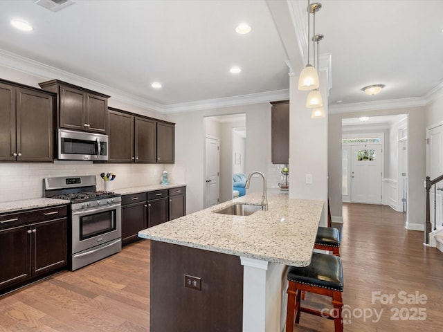 kitchen with appliances with stainless steel finishes, light wood-style floors, a sink, dark brown cabinets, and a kitchen breakfast bar