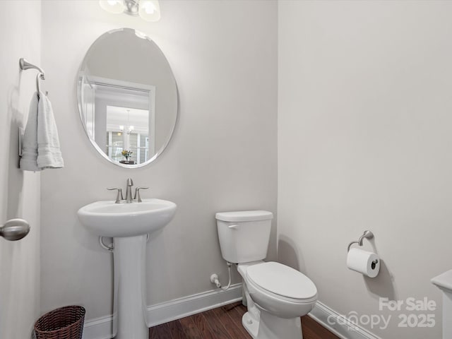 bathroom with baseboards, toilet, wood finished floors, a chandelier, and a sink