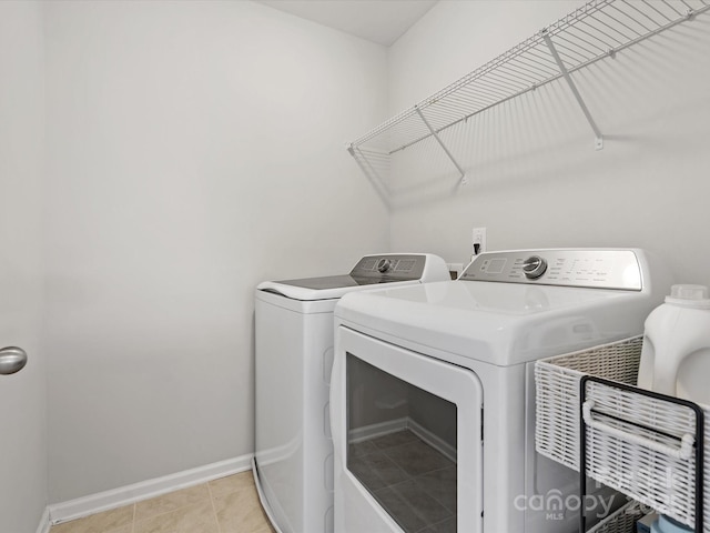 washroom featuring washing machine and dryer, laundry area, baseboards, and light tile patterned floors