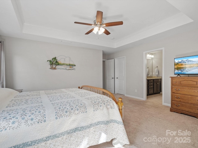 bedroom featuring connected bathroom, light colored carpet, a ceiling fan, baseboards, and a tray ceiling