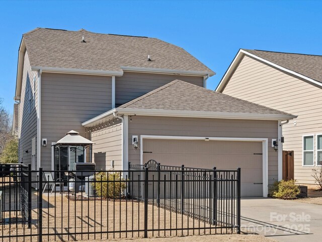 view of front of home featuring an attached garage, fence, concrete driveway, a gazebo, and roof with shingles