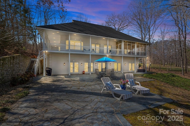 back of property at dusk featuring french doors, a patio area, a balcony, and stucco siding