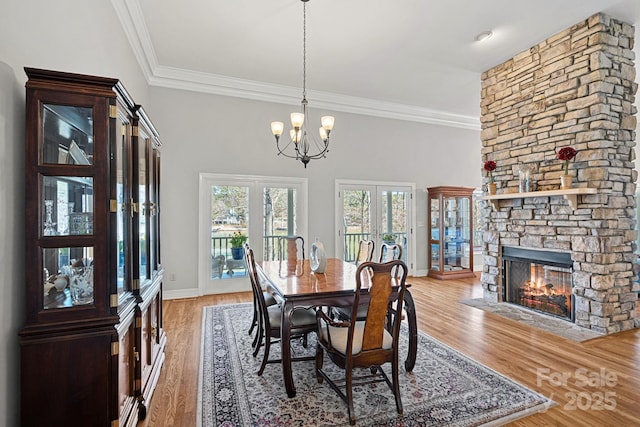 dining space with light wood-style floors, a fireplace, an inviting chandelier, and ornamental molding