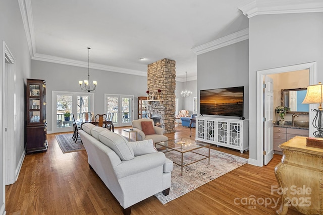 living room with crown molding, an inviting chandelier, a stone fireplace, wood finished floors, and baseboards