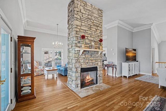 living area with baseboards, ornamental molding, wood finished floors, an inviting chandelier, and a stone fireplace