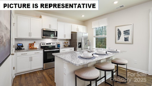 kitchen featuring tasteful backsplash, appliances with stainless steel finishes, a kitchen island with sink, a sink, and a kitchen breakfast bar