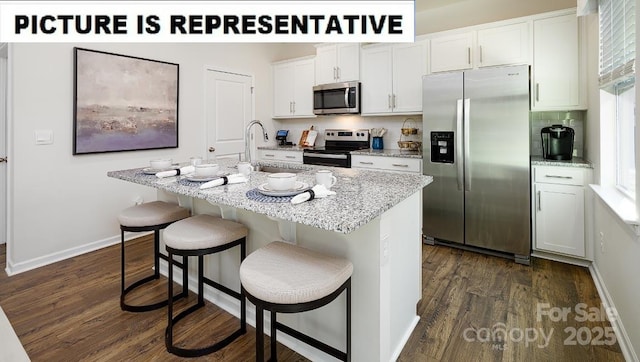 kitchen with a breakfast bar, dark wood finished floors, stainless steel appliances, white cabinets, and an island with sink