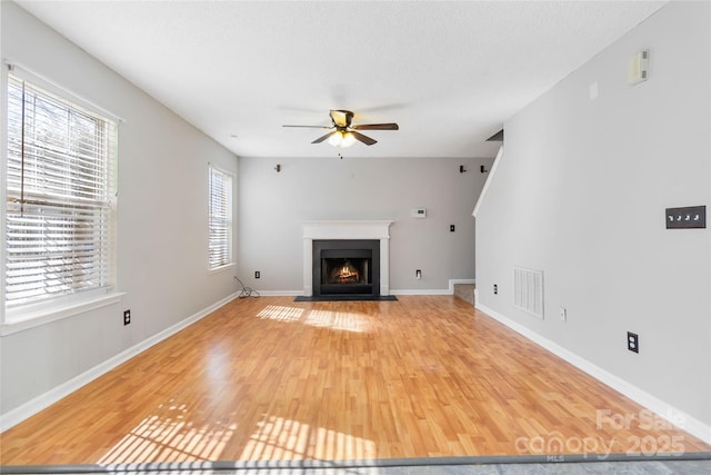 unfurnished living room with light wood-type flooring, a fireplace with flush hearth, visible vents, and baseboards