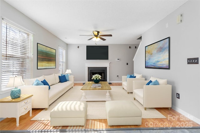 living room featuring ceiling fan, a textured ceiling, a fireplace, and wood finished floors