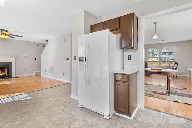 kitchen featuring a textured ceiling, a fireplace with flush hearth, a ceiling fan, open floor plan, and white fridge with ice dispenser