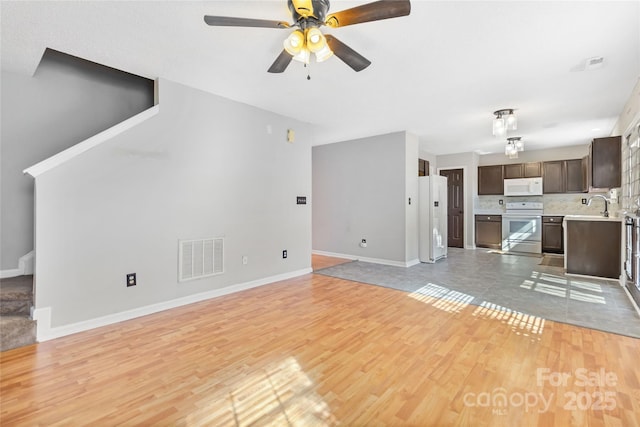 unfurnished living room featuring stairs, light wood-type flooring, a sink, and visible vents