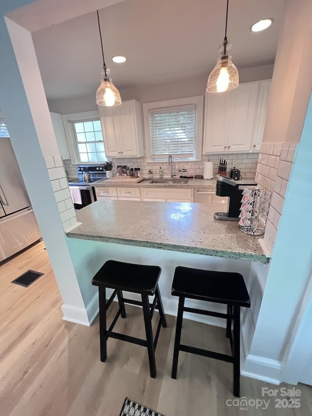 kitchen with light stone counters, a sink, visible vents, and white cabinetry