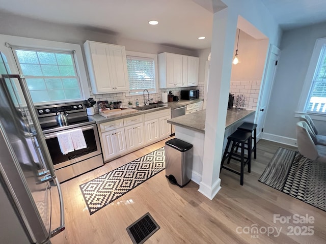 kitchen featuring stainless steel appliances, visible vents, light wood-style floors, white cabinets, and a sink