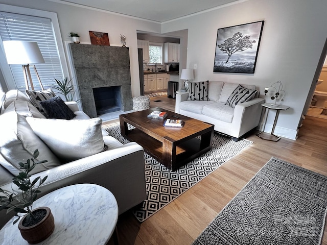 living area featuring ornamental molding, a fireplace, light wood-style flooring, and baseboards