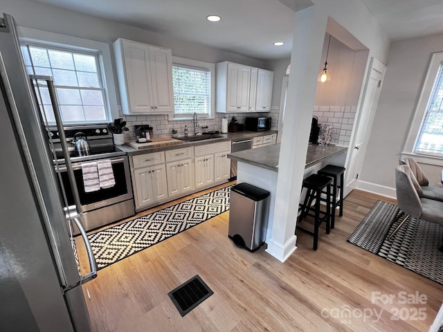 kitchen with light wood finished floors, visible vents, stainless steel appliances, white cabinetry, and a sink