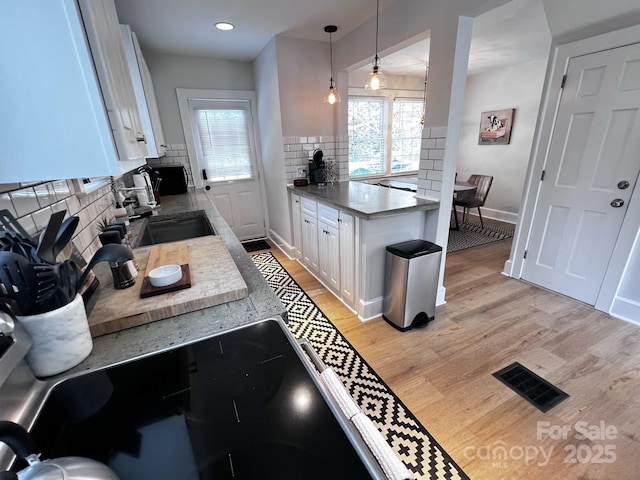 kitchen with visible vents, backsplash, light wood-style flooring, white cabinetry, and a sink