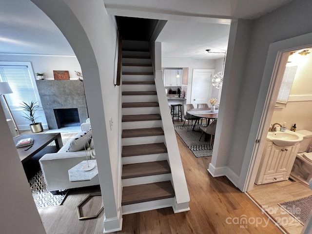 stairway featuring arched walkways, a fireplace, baseboards, and wood finished floors