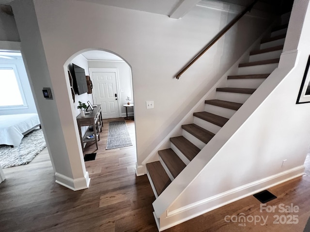 staircase featuring arched walkways, wood finished floors, and baseboards