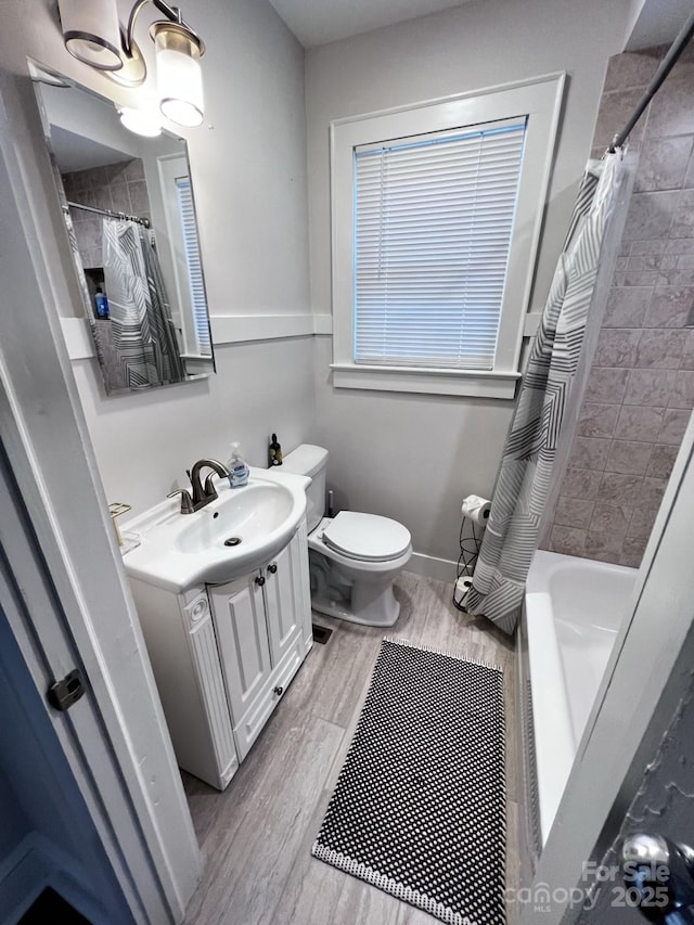 bathroom featuring toilet, wood finished floors, vanity, baseboards, and shower / bath combo