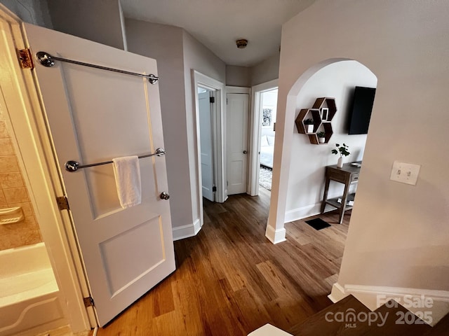 hall with arched walkways, wood finished floors, and baseboards