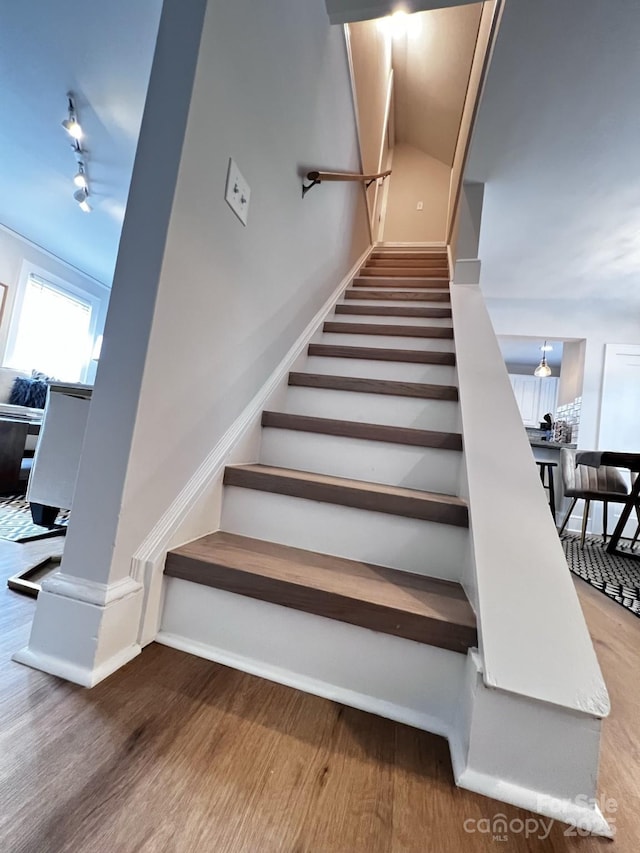 stairs featuring rail lighting, baseboards, and wood finished floors