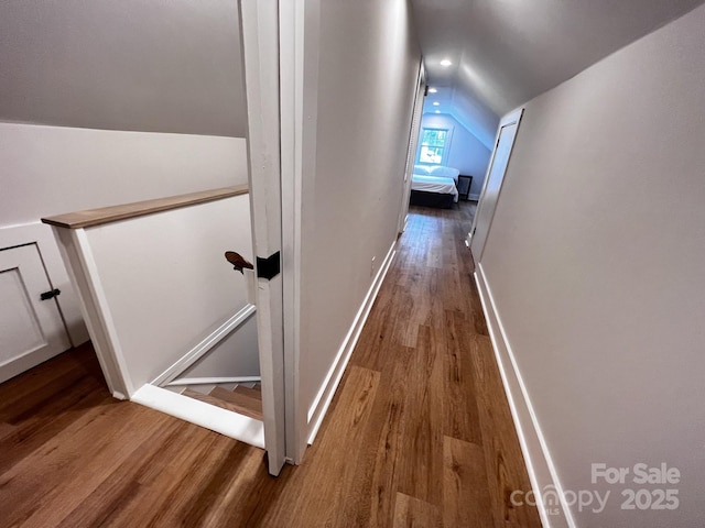 hallway featuring lofted ceiling, baseboards, wood finished floors, and an upstairs landing