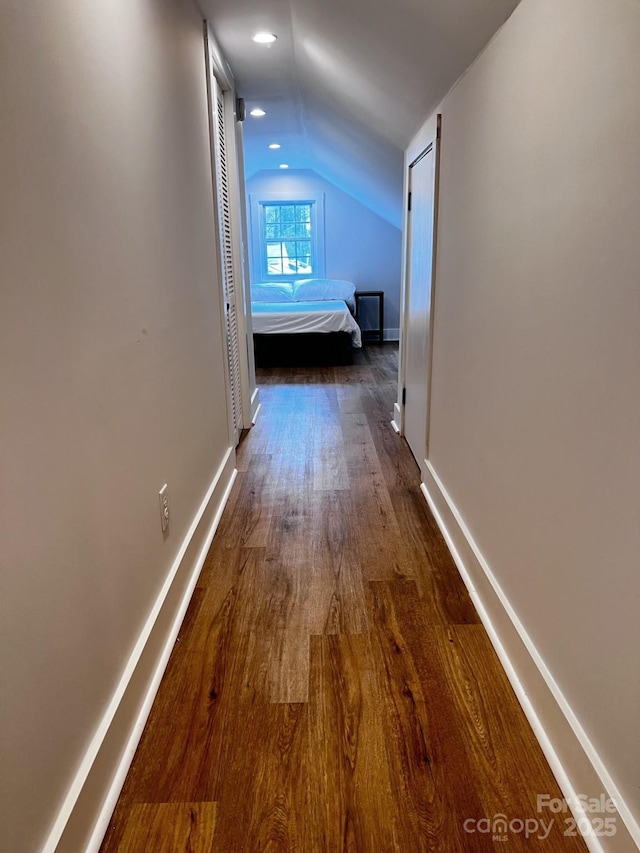 corridor with lofted ceiling, baseboards, and wood finished floors