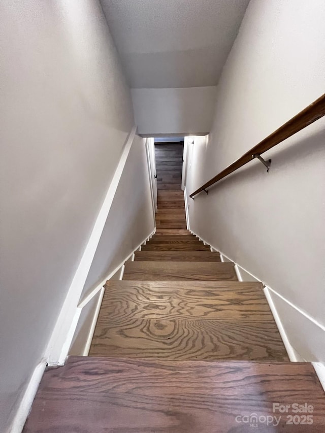 stairway with a textured ceiling and wood finished floors