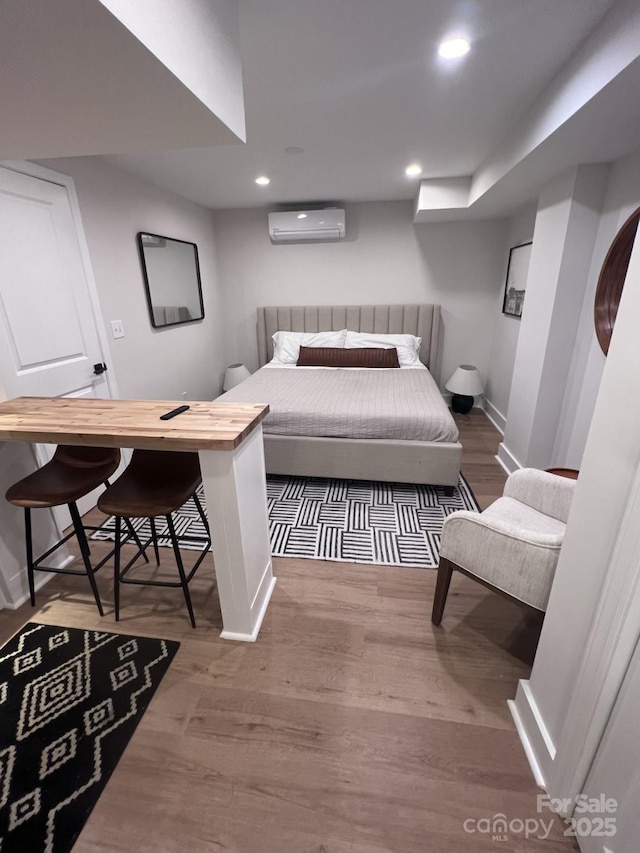 bedroom featuring recessed lighting, a wall mounted air conditioner, baseboards, and wood finished floors