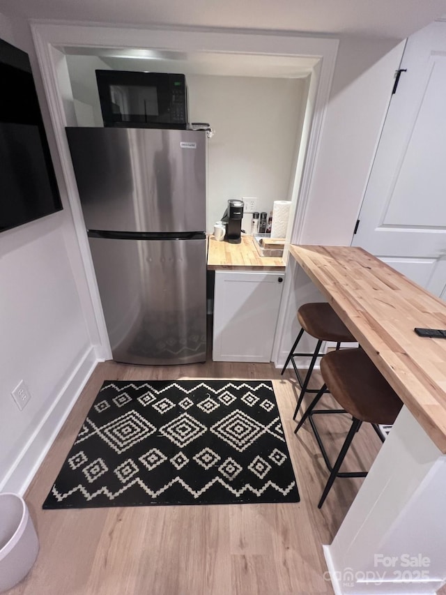 kitchen with freestanding refrigerator, black microwave, wood counters, and wood finished floors