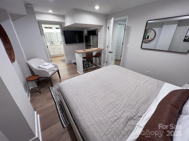 bedroom featuring recessed lighting, ensuite bathroom, freestanding refrigerator, wood finished floors, and baseboards