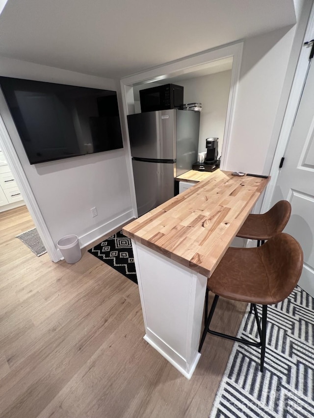 kitchen with butcher block counters, light wood-style floors, freestanding refrigerator, black microwave, and baseboards