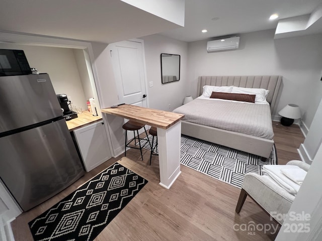 bedroom featuring freestanding refrigerator, wood finished floors, baseboards, and a wall mounted AC