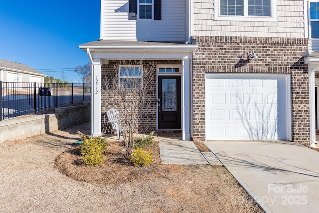 property entrance with driveway, brick siding, an attached garage, and fence