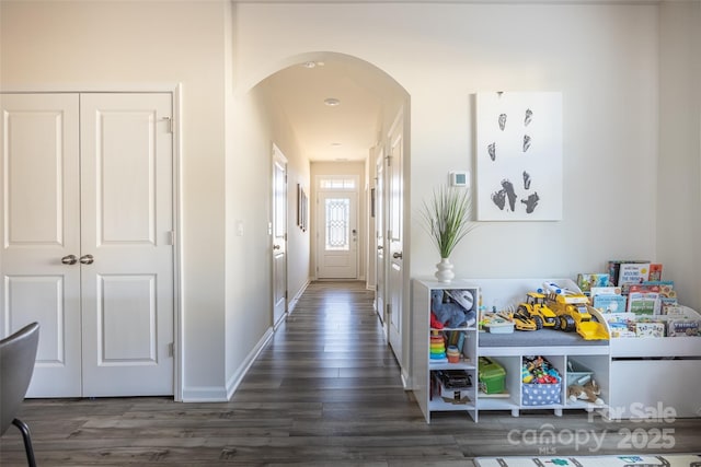 hallway with baseboards, arched walkways, and dark wood-style flooring