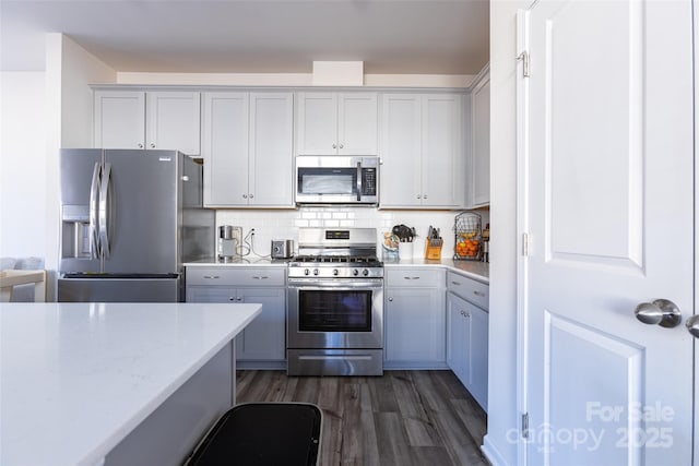 kitchen with decorative backsplash, dark wood-style floors, appliances with stainless steel finishes, light countertops, and gray cabinetry